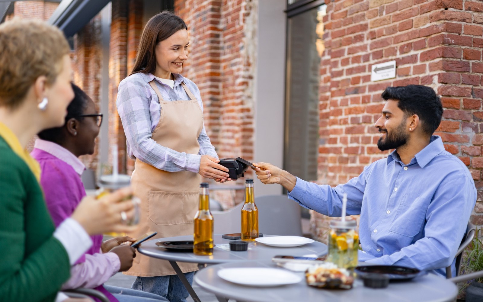 A waiter taking a card payment from a seated guest at a restaurant table